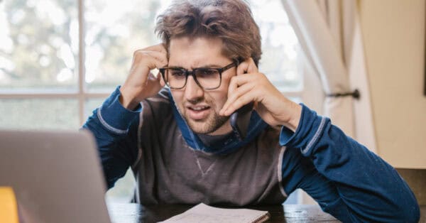 confused man looking at computer screen and on the phone